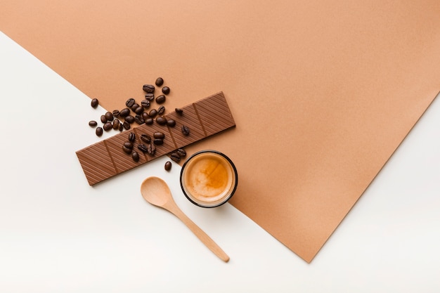 Granos de café tostados; barra de chocolate y vaso de café con una cuchara en el fondo