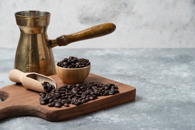 Granos de café tostados oscuros y cafetera sobre tabla de cortar de madera.