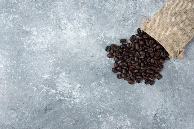 Granos de café tostados de saco de arpillera sobre mármol.