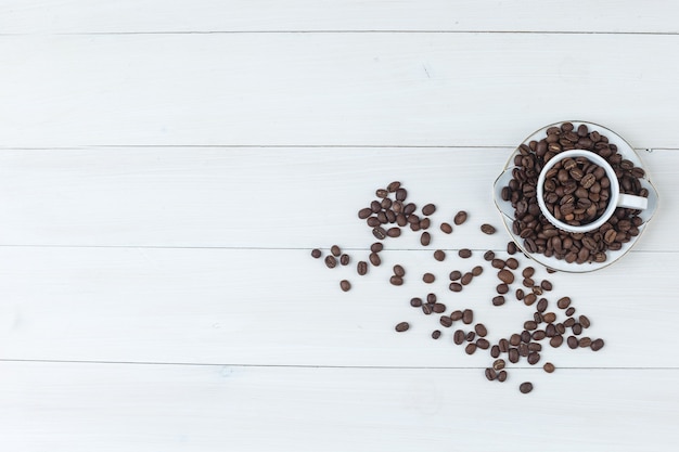 Granos de café en la vista superior de la taza y el platillo sobre un fondo de madera