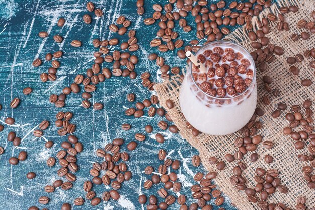 Granos de chocolate y café con una taza de bebida en azul.