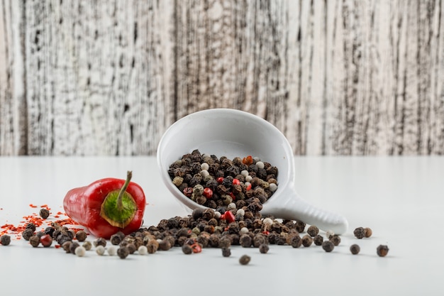 Foto gratuita granos de pimienta mezclados en un plato con vista lateral de pimiento rojo en la pared de grunge blanco y madera