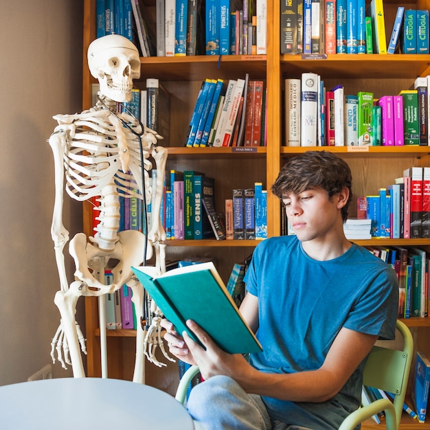 Grave adolescente leyendo cerca de esqueleto