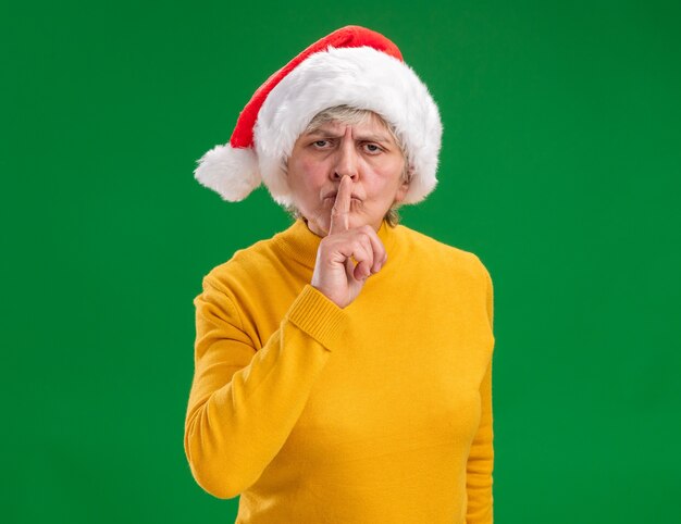 Grave anciana con gorro de Papá Noel haciendo gesto de silencio aislado sobre fondo púrpura con espacio de copia