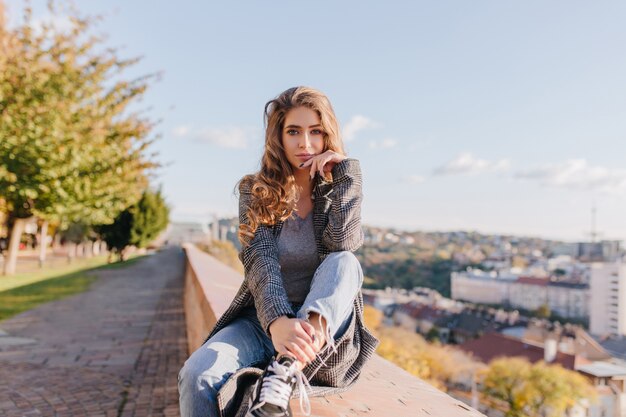 Grave chica bien vestida con cabello rizado apuntando la cara con la mano