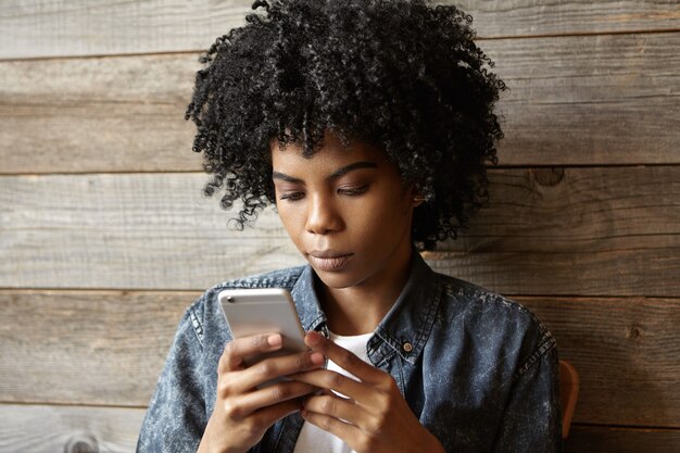 Grave hermosa niña afroamericana leyendo noticias mientras navega por internet en el teléfono móvil