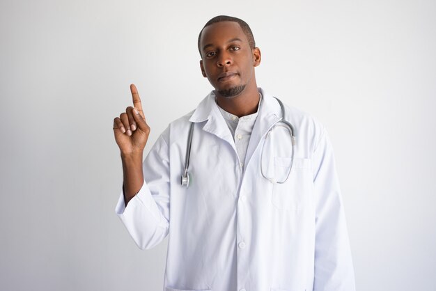 Grave hombre médico de pelo oscuro apuntando hacia arriba.