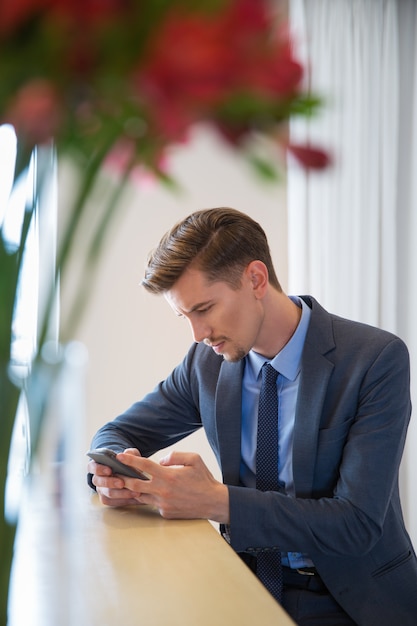 Foto gratuita grave hombre de negocios adulto que se sienta y smartphone