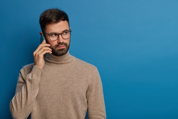 Grave joven barbudo habla por teléfono, llama a alguien a través de un dispositivo moderno