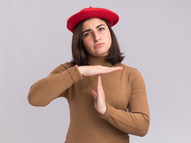 Grave joven bastante caucásica con sombrero de boina gesticulando señal de tiempo de espera