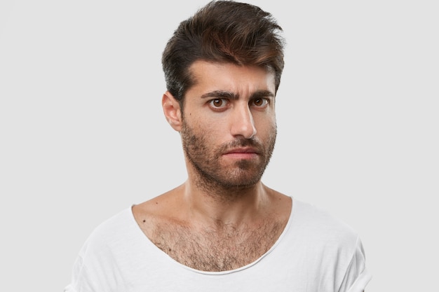 Grave joven caucásico con barba oscura y gruesa, corte de pelo de moda, ropa casual, modelos contra el espacio en blanco