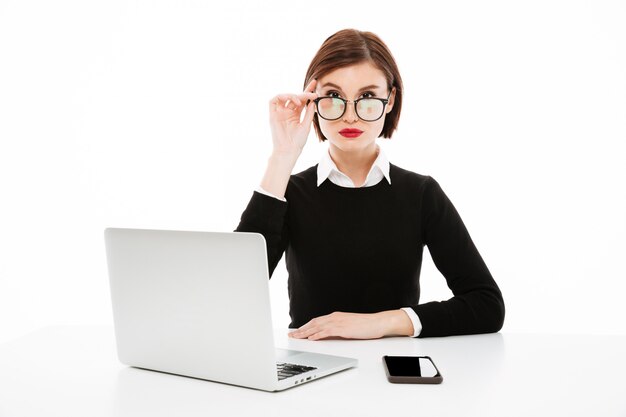 Grave joven dama de negocios con gafas usando la computadora portátil