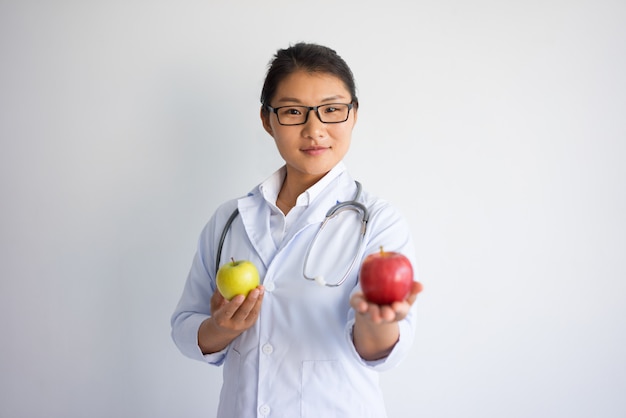 Grave joven doctora asiática ofreciendo manzana roja. Concepto de nutrición saludable.