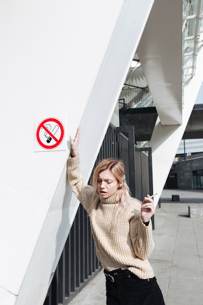 Foto gratuita grave jovencita rubia con cigarrillo al aire libre