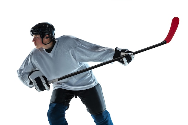 Grave. Jugador de hockey masculino joven con el palo en la cancha de hielo y pared blanca. Deportista con equipo y casco practicando. Concepto de deporte, estilo de vida saludable, movimiento, movimiento, acción.