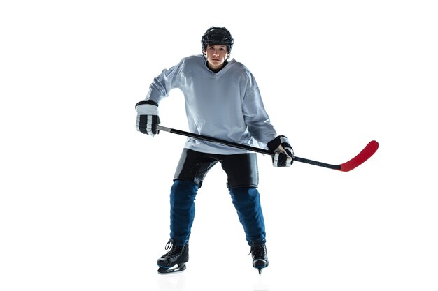 Grave. Jugador de hockey masculino joven con el palo en la cancha de hielo y pared blanca. Deportista con equipo y casco practicando. Concepto de deporte, estilo de vida saludable, movimiento, movimiento, acción.