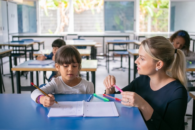 Grave maestro de escuela primaria ayudando a la niña a hacer frente a su tarea