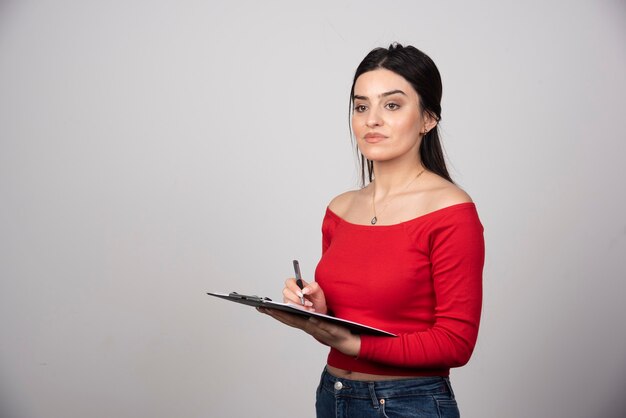 Grave mujer escribiendo en un portapapeles y mirando a otro lado.