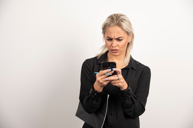 Grave mujer mirando por teléfono móvil y sosteniendo un portapapeles. Foto de alta calidad