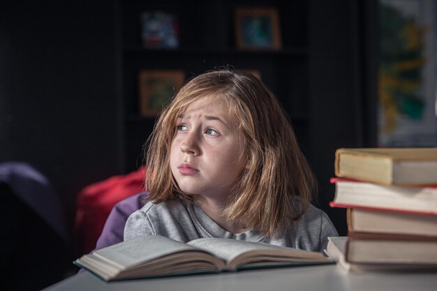 Grave niña leyendo un libro sentado en la mesa