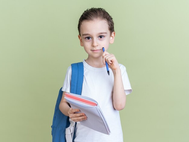 Grave niño con mochila sosteniendo el bloc de notas tocando la cara con la pluma