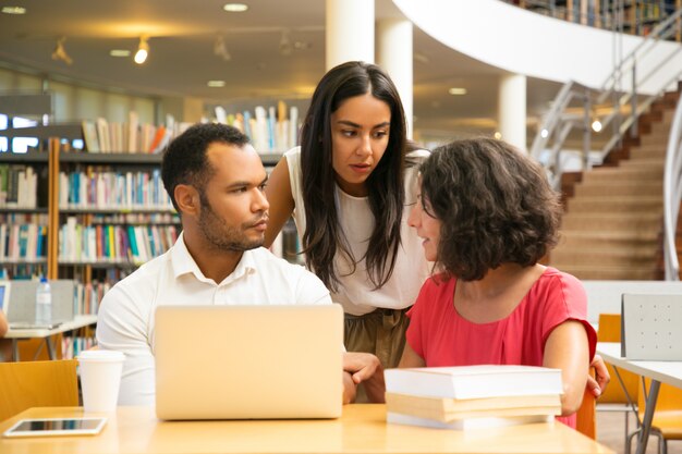 Graves estudiantes sentados a la mesa en la biblioteca con laptop