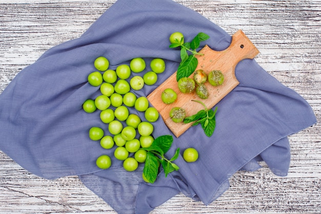 Greengages picantes con hojas en una pequeña tabla de cortar de madera plana sobre una madera blanca y un paño de picnic