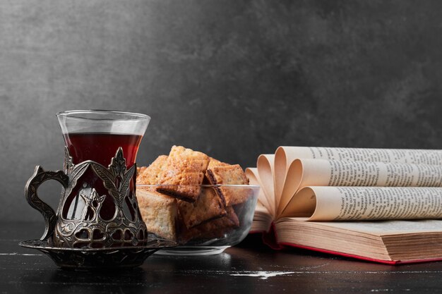 Grietas crujientes en una taza de vidrio sobre fondo negro con un vaso de té.