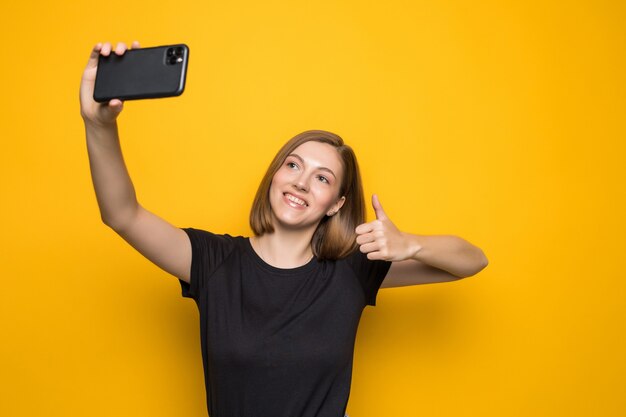 Gritando a mujer joven tomando una foto selfie en amarillo