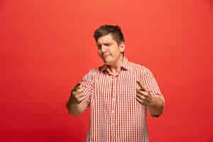 Foto gratuita gritos, odio, rabia. hombre enojado emocional llorando gritando sobre fondo rojo de estudio. rostro joven y emocional. retrato masculino de medio cuerpo.