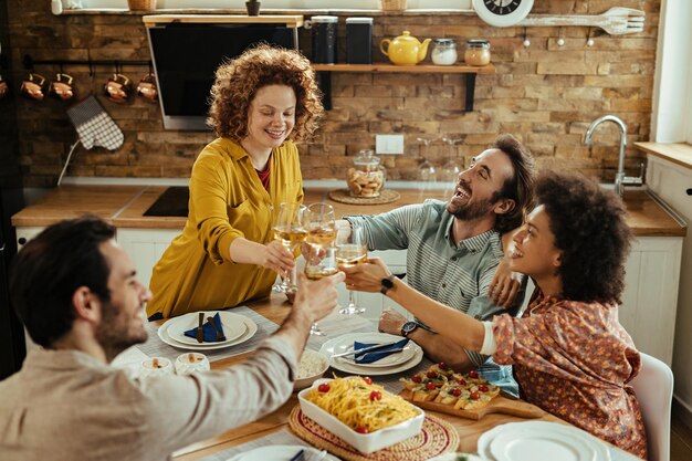 Grupo de adultos jóvenes felices brindando y divirtiéndose mientras almuerzan juntos en el comedor