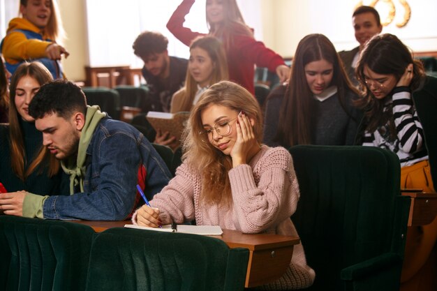 El grupo de alegres estudiantes felices sentados en una sala de conferencias antes de la lección