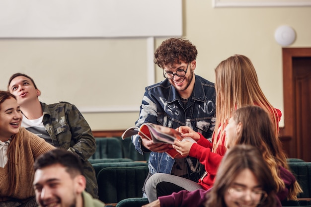 El grupo de alegres estudiantes felices sentados en una sala de conferencias antes de la lección