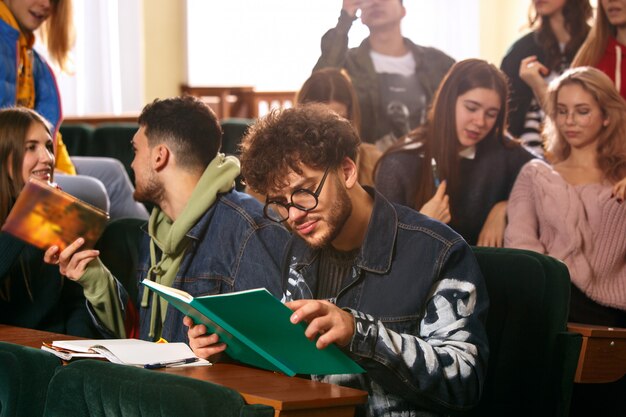 El grupo de alegres estudiantes felices sentados en una sala de conferencias antes de la lección