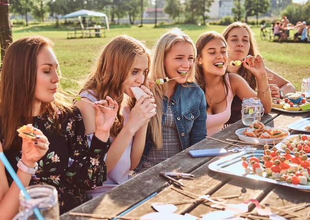 Grupo de amigas comiendo en la mesa juntas celebrando un cumpleaños en el parque al aire libre.