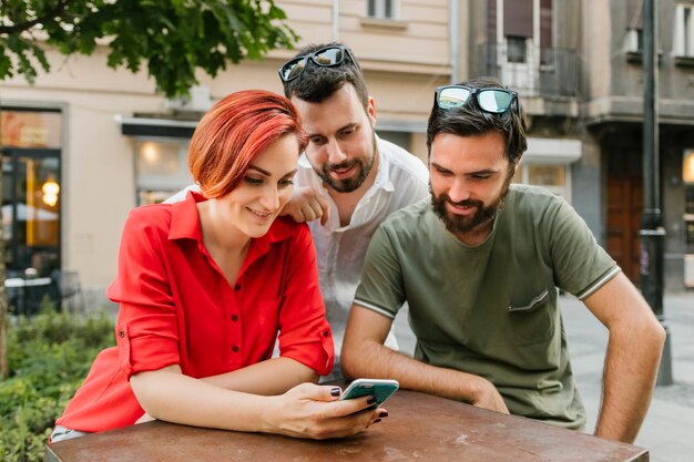 Grupo de amigos adultos que usan teléfono inteligente en la calle juntos
