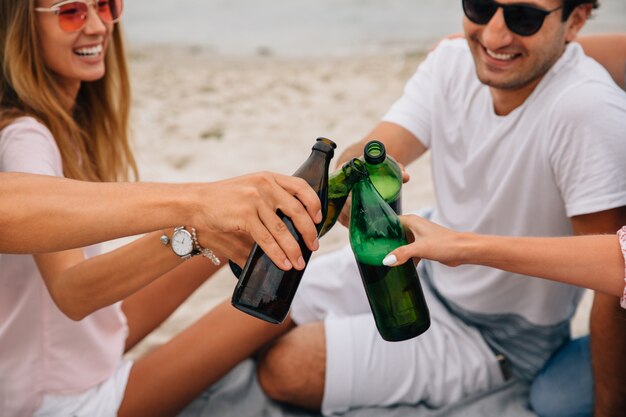 Grupo de amigos alegres haciendo un brindis, mientras se relaja en la playa, sonriendo alegremente