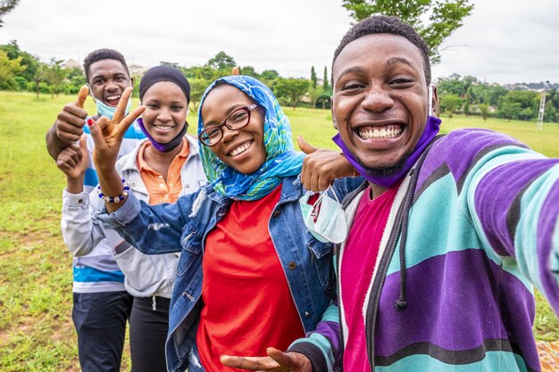 Grupo de amigos alegres con mascarillas tomando un selfie en un parque