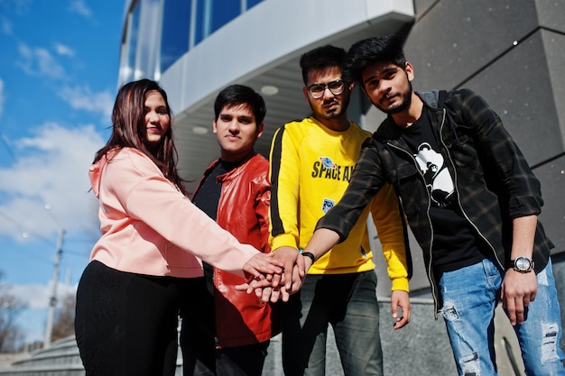 Grupo de amigos asiáticos se paran en las escaleras al aire libre contra un edificio moderno y se dan la mano juntos