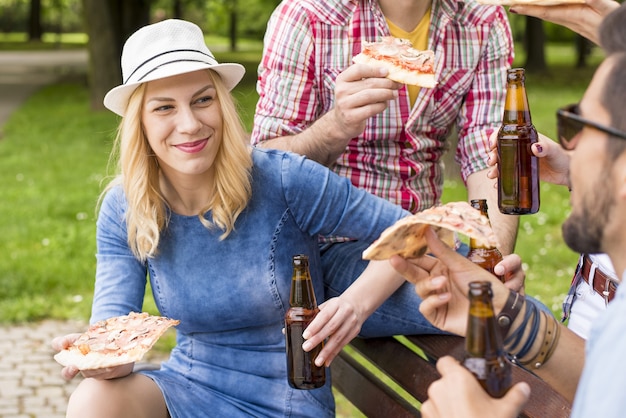 Grupo de amigos caucásicos sentados en el banco y disfrutando de su cerveza en el parque