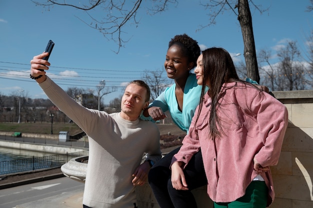 Grupo de amigos celebrando el levantamiento de las restricciones de uso de mascarillas tomándose un selfie juntos al aire libre