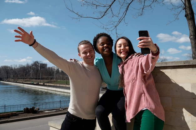 Grupo de amigos celebrando el levantamiento de las restricciones de uso de mascarillas tomándose un selfie juntos al aire libre