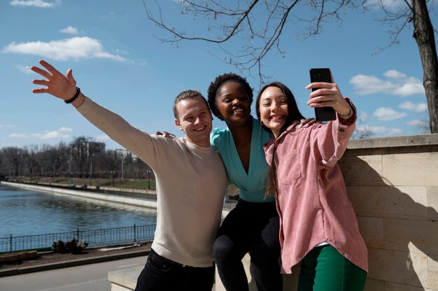 Grupo de amigos celebrando el levantamiento de las restricciones de uso de mascarillas tomándose un selfie juntos al aire libre