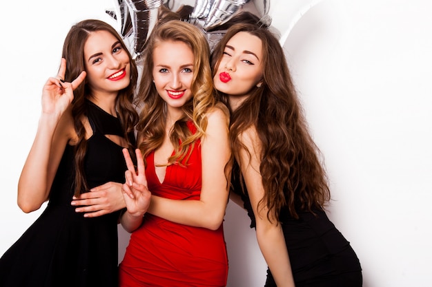 Grupo de amigos celebrando posando en el estudio. Tres mujeres bonitas se divierten, guiñando un ojo, riendo y mirando a la cámara.