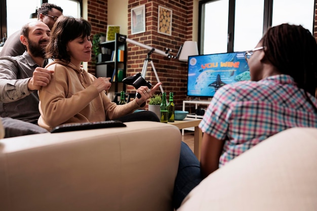 Grupo de amigos cercanos jugando videojuegos de simulación espacial en una consola de juegos moderna. Adultos jóvenes sentados en un sofá en casa mientras disfrutan del tiempo juntos y de actividades de ocio divertidas en un dispositivo de entretenimiento.