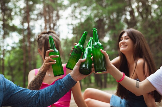 Grupo de amigos chocan botellas de cerveza durante el picnic en el bosque de verano