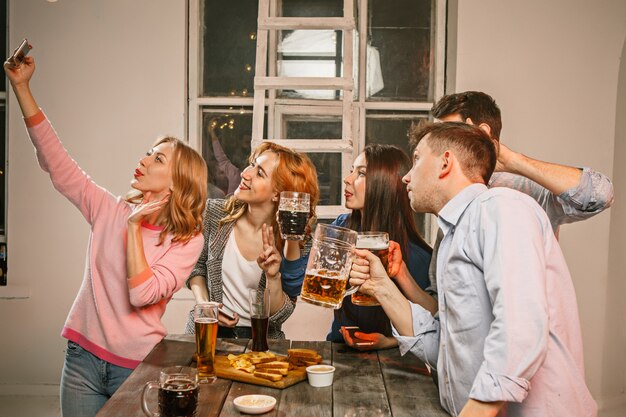 Grupo de amigos disfrutando de bebidas por la noche con cerveza en la mesa de madera