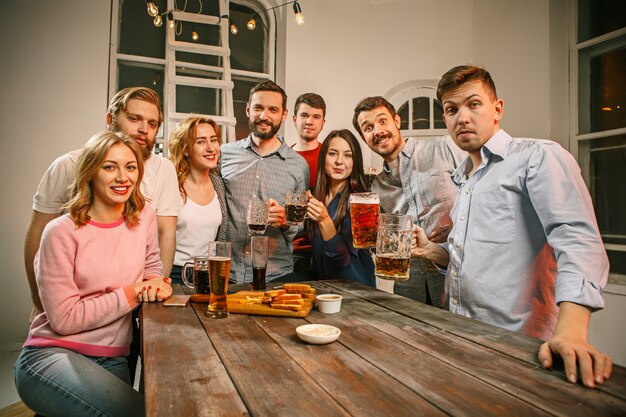 Grupo de amigos disfrutando de bebidas por la noche con cerveza en la mesa de madera