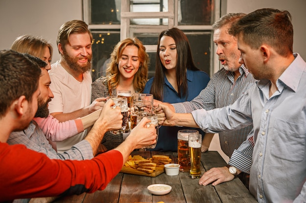 Grupo de amigos disfrutando de bebidas por la noche con cerveza en la mesa de madera