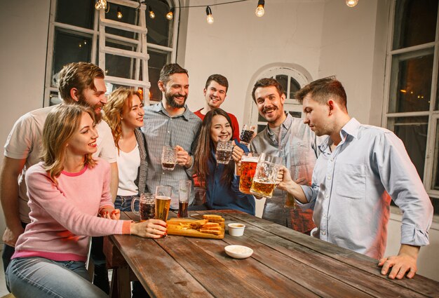 Grupo de amigos disfrutando de bebidas por la noche con cerveza en la mesa de madera